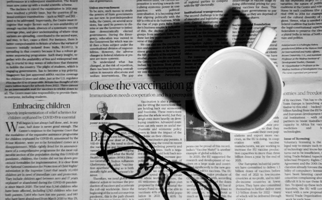 Un periódico extendido abierto sobre una mesa, con una taza de café y un par de gafas colocados encima.